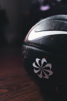 Black basketball with distinctive white logo on a wooden floor. Perfect for sports themes.