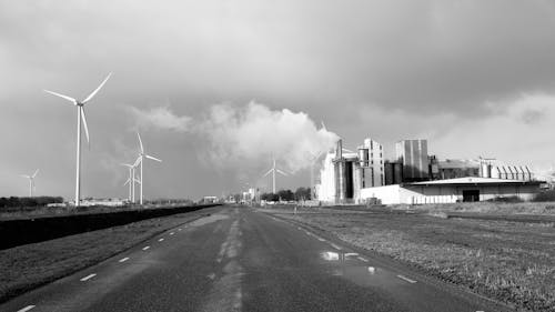 A Grayscale of Windmills and a Factory by the Road