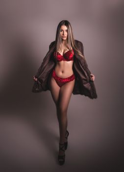 Elegant studio shot of woman posing in red lingerie with a faux fur coat, exuding confidence.