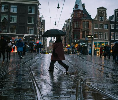 A person walks with an umbrella on a rainy day in Amsterdam's historic streets.