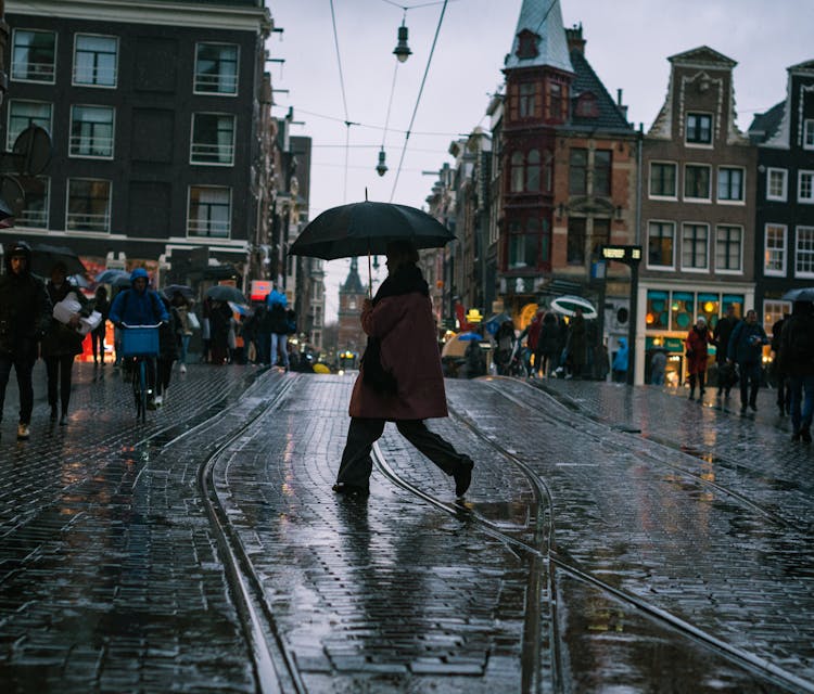 A Person Using An Umbrella While Crossing The Street