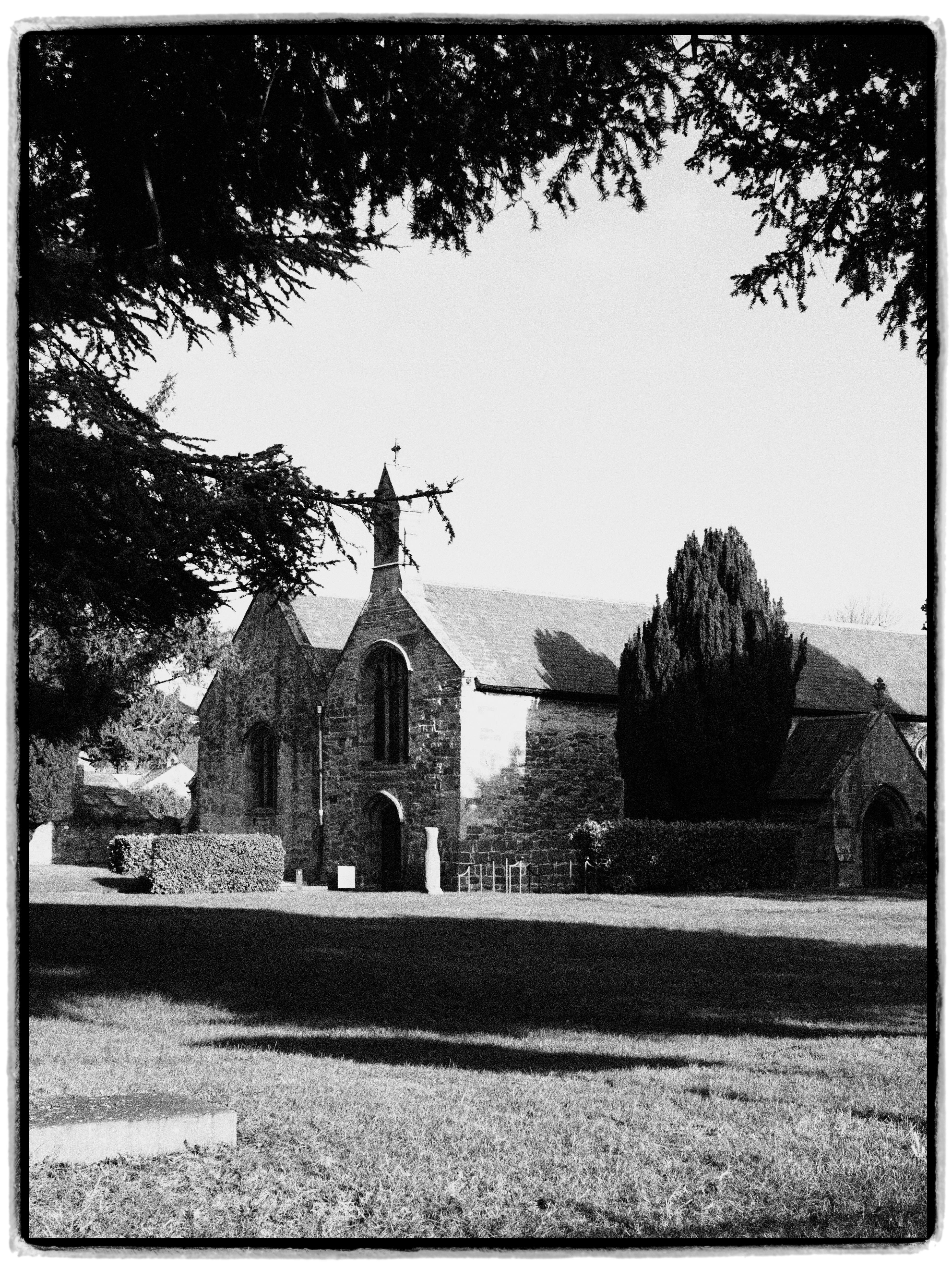 Serene black and white photo of a historic stone church surrounded by trees.
