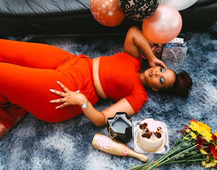 A fashionable woman celebrating with balloons, birthday cake, and flowers in a vibrant indoor setting.
