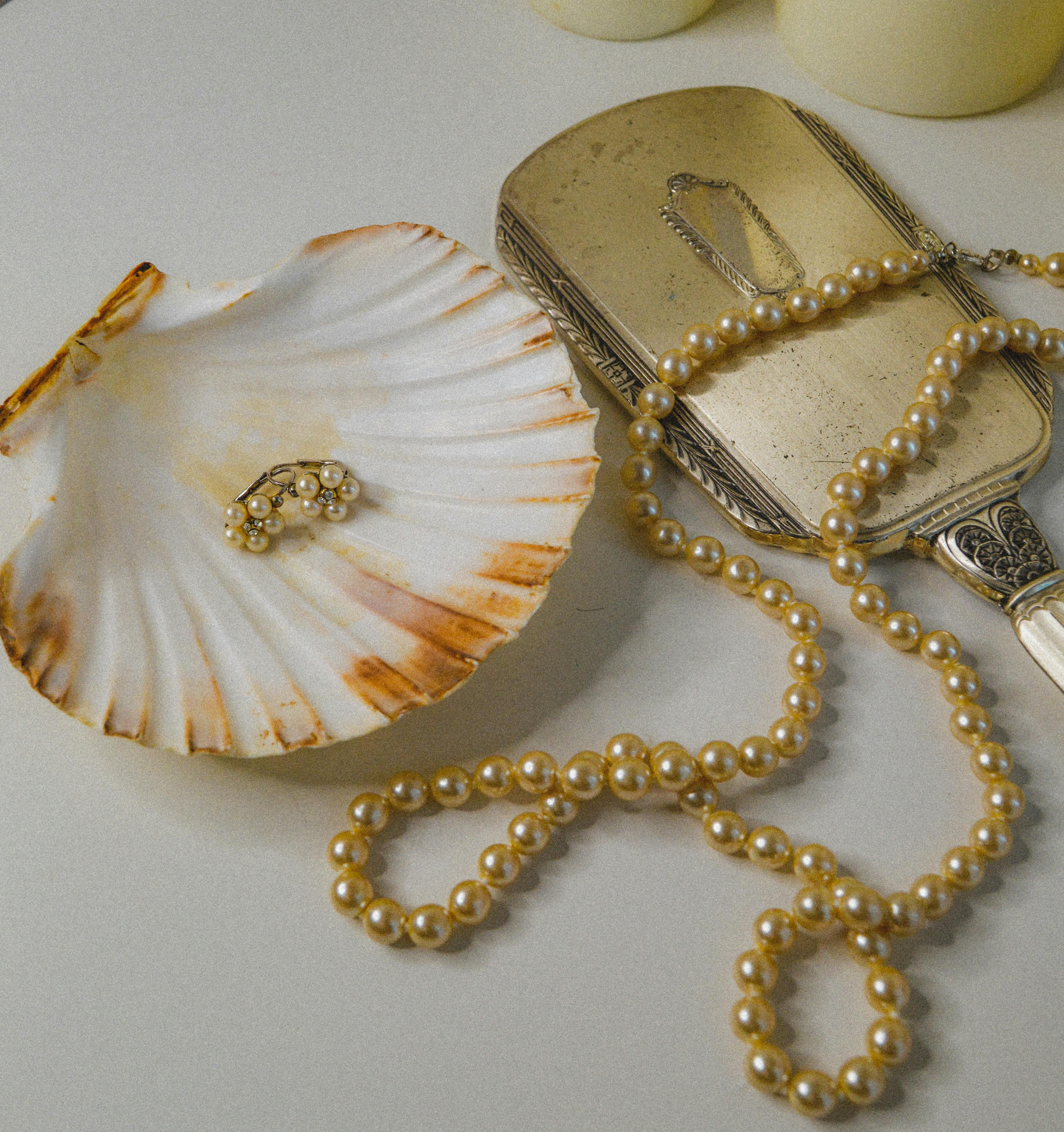Close-up of luxurious pearl necklace and earring on elegant shell and antique mirror.