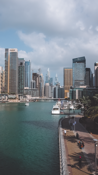 Panoramic view of the iconic Dubai Marina skyline with yachts and a bustling walkway.