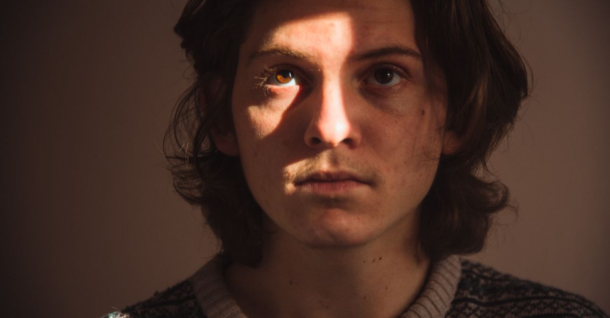 Moody portrait of a teenage boy in sunlight highlighting eyes and features.