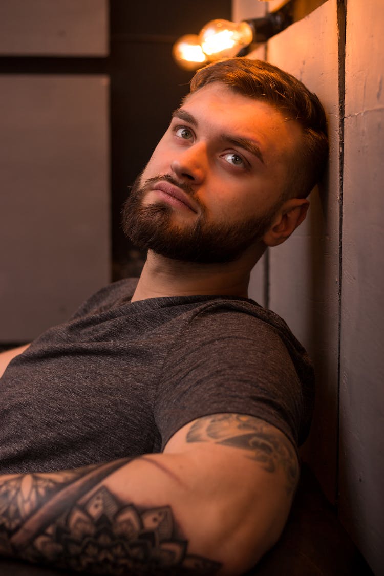 Man With Tattoo On An Arm Leaning Against A Wall