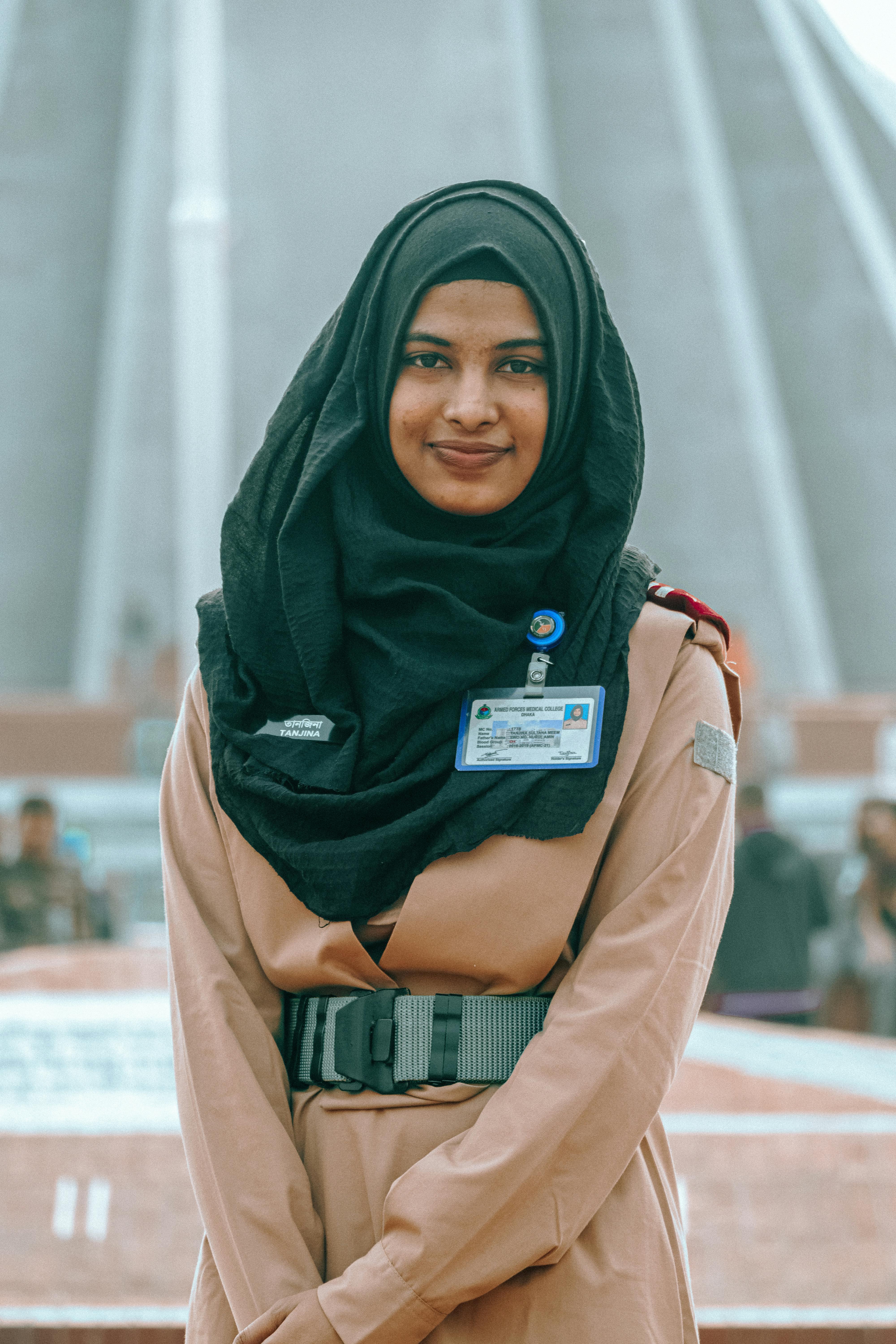 Portrait of a Muslim woman in uniform with hijab at a Dhaka landmark. Bright and confident.