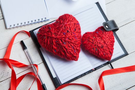 Two heart-shaped yarn decorations rest on an open notebook, symbolizing love and creativity.