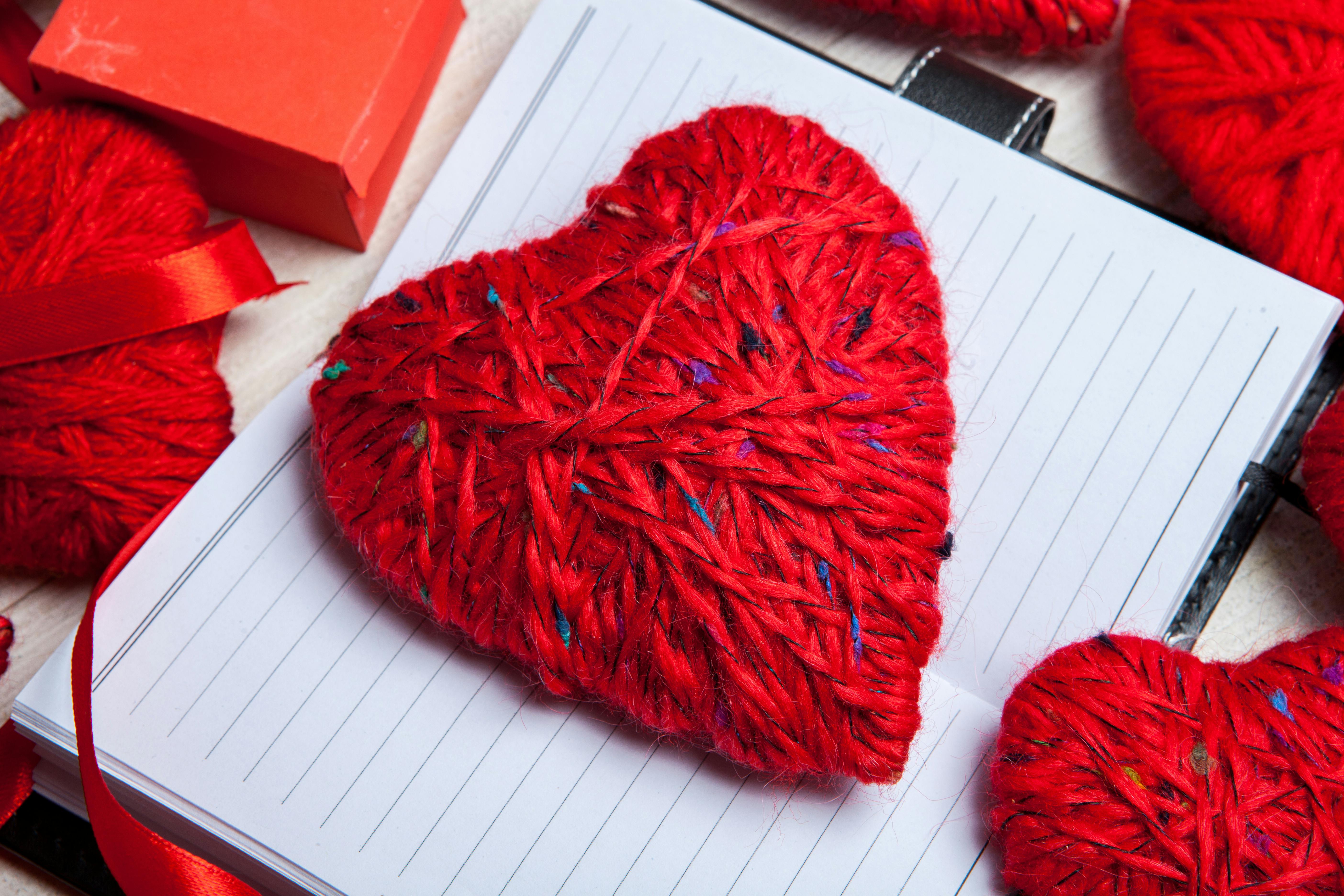 A vibrant red yarn heart sits atop an open notebook, accompanied by a red gift box, evoking warmth and sentiment.
