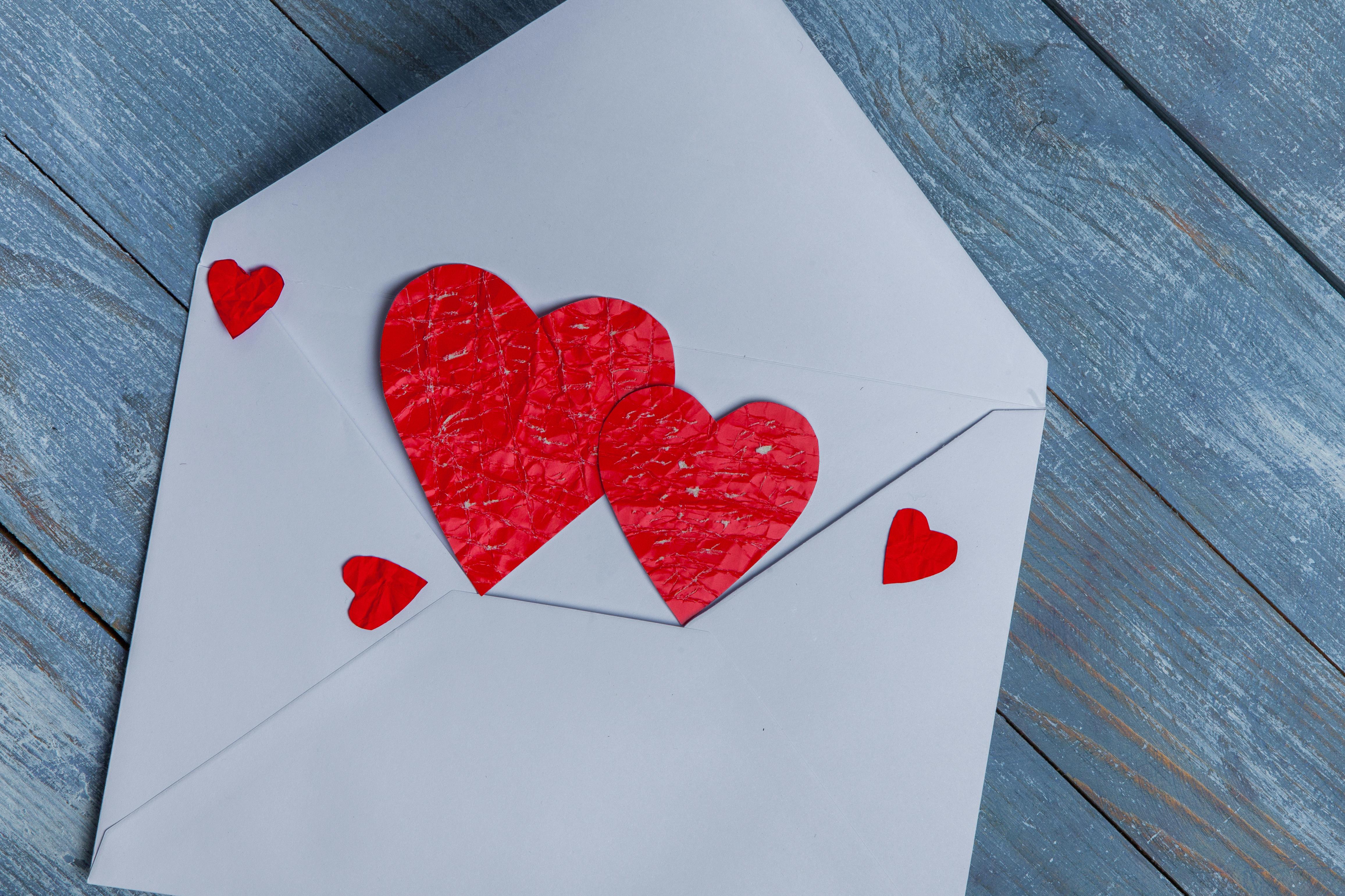 Close-up of a white envelope with red heart cutouts symbolizing romance and love.