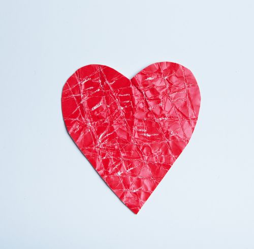 Free A close-up of a crumpled red heart-shaped paper cutout against a light gray background. Stock Photo