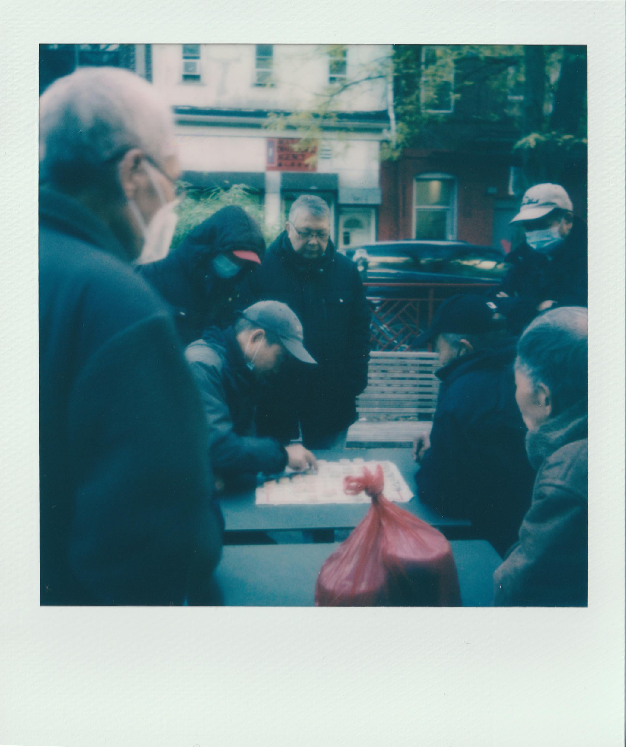 Elderly men gathered around a board game table in an outdoor Boston park, enjoying a social afternoon.