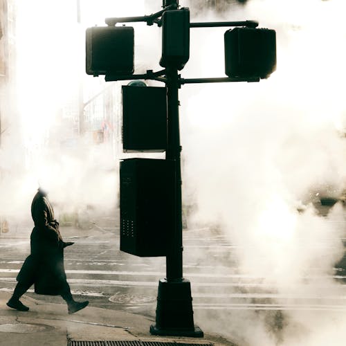 A Person in a Coat Walking on a Sidewalk during a Foggy Day