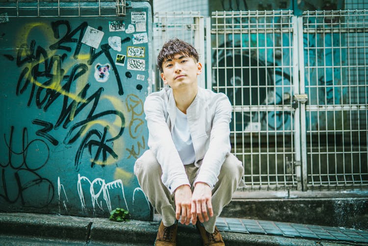 Male Teenager Crouching On Edge Of Road With Graffiti In Background