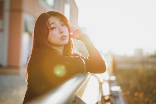 Free A beautiful woman is leaning on a handrail, bathed in warm sunlight during the golden hour. Stock Photo