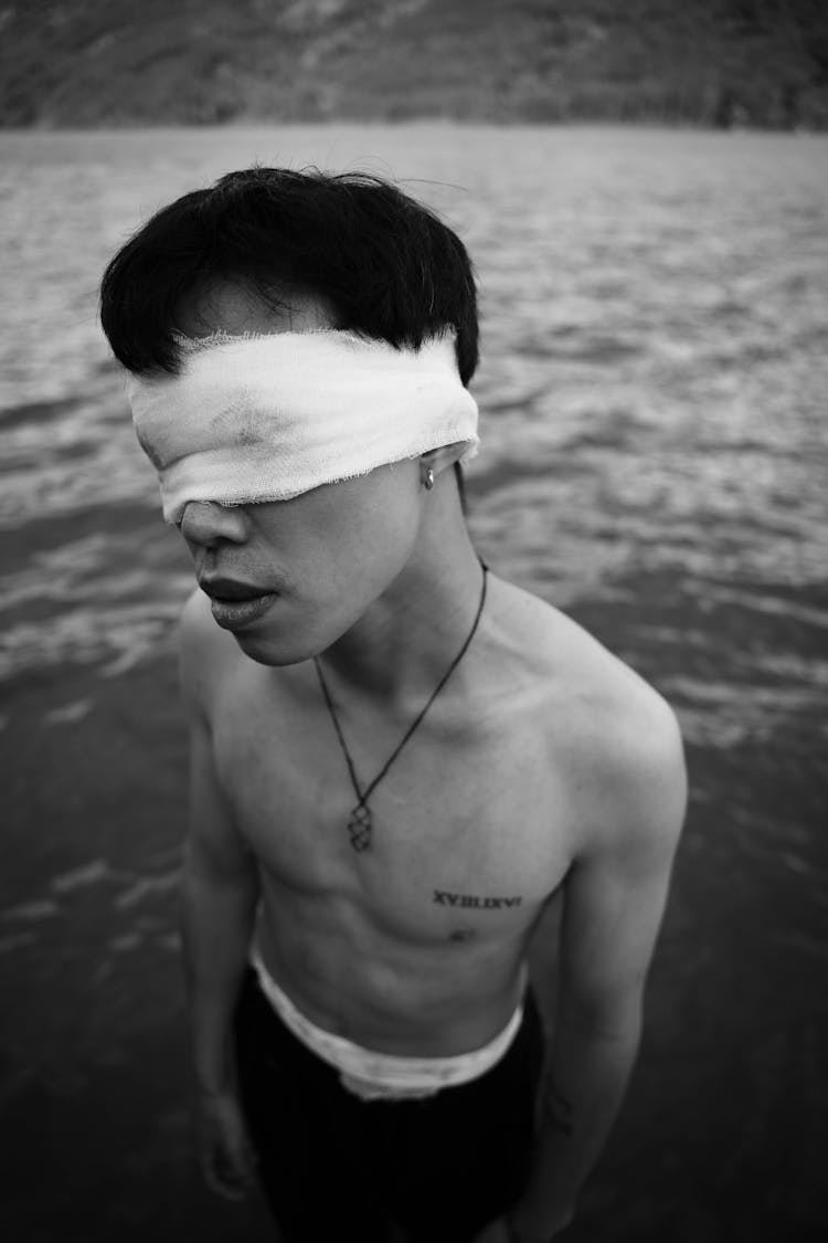 Young Man With Eyes Covered With Band Standing By Lake