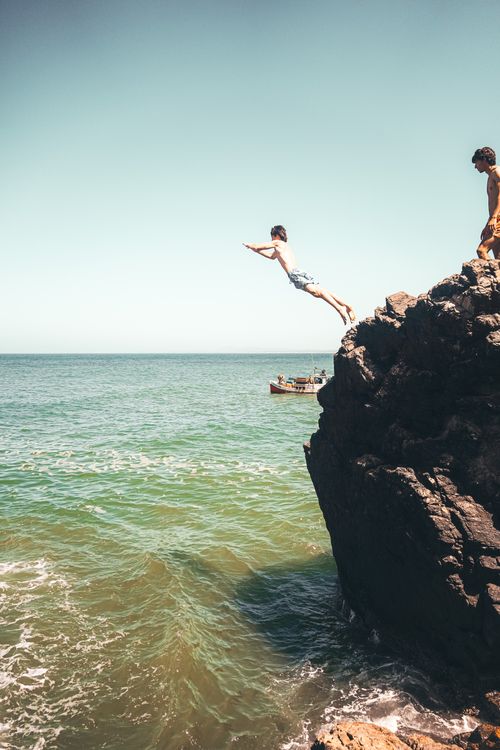 Free Young men cliff diving into ocean at Punta del Este, Uruguay, capturing adventurous summer vibes. Stock Photo