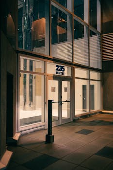 A sleek glass entrance of an office building at night, showcasing modern architectural design.