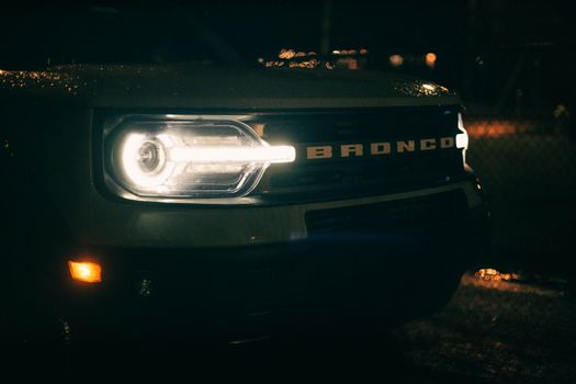 Detailed close-up of a Ford Bronco headlight and grille at night.