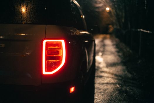 Close-up of a car's tail light on a rainy night, illuminating a wet street.