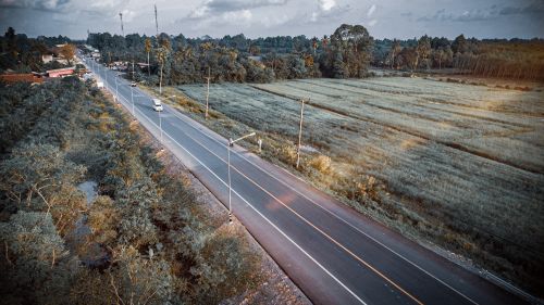 Free Stunning aerial view showcasing a rural asphalt road flanked by lush green fields. Stock Photo