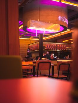 A vibrant restaurant interior featuring neon lights and modern furniture with people dining.