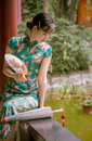 Woman in Blue Green and Red Floral Dress Sitting on White Chair Reading Book