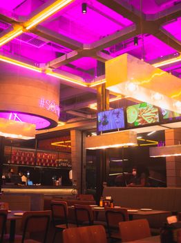 Contemporary restaurant interior featuring vibrant neon lights and modern decor, creating a lively ambiance.