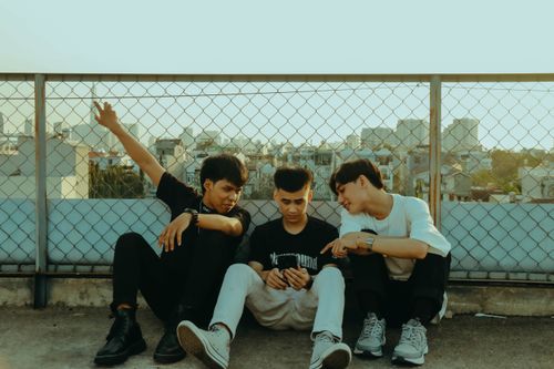 Free Three teenagers sitting together on a rooftop, enjoying city skyline views. Urban friendship moment. Stock Photo