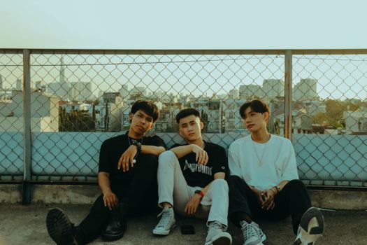 Three teenage friends sitting on a rooftop with city skyline backdrop, enjoying the evening.