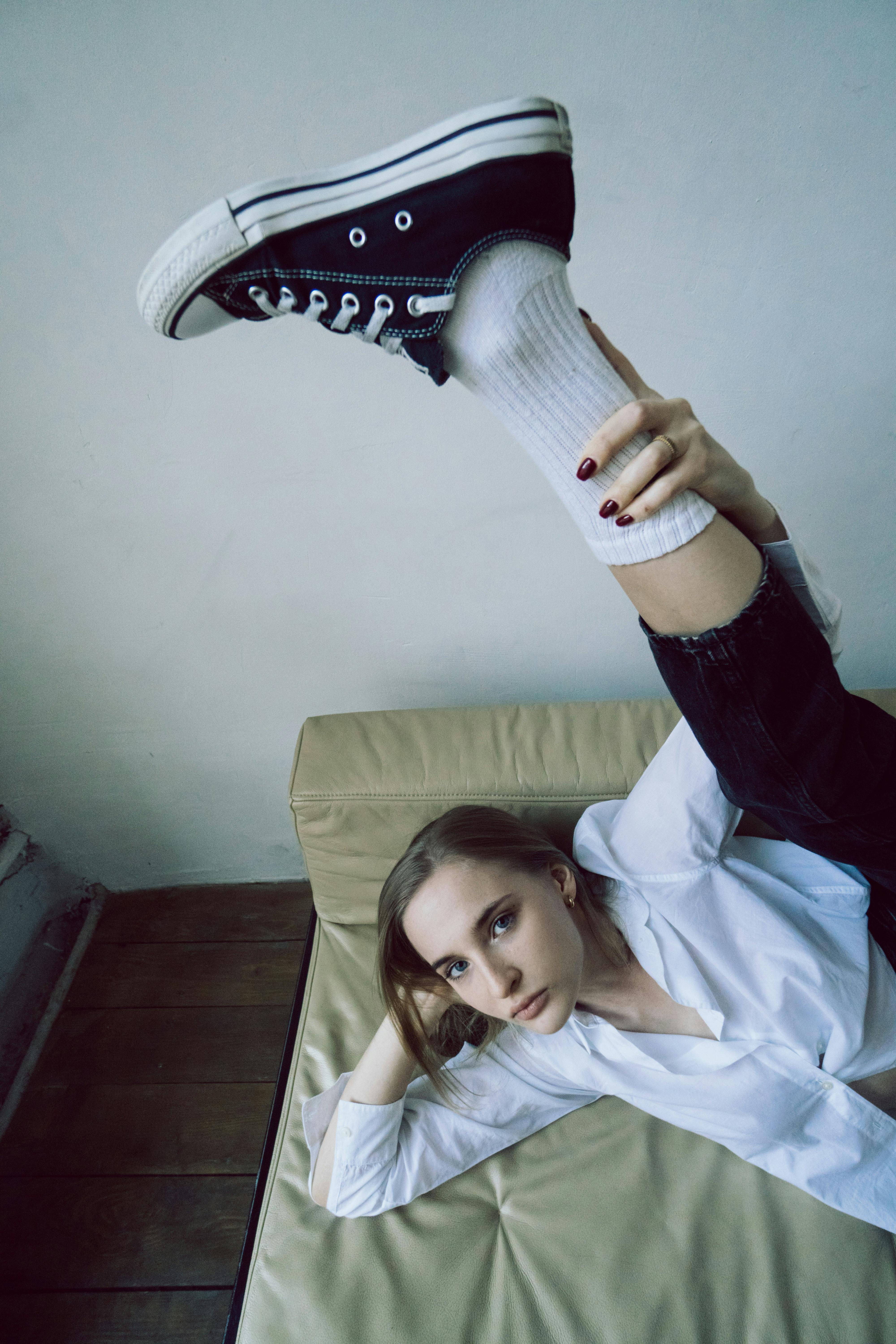 Stylish young woman posing indoors with leg elevated creatively on a couch.