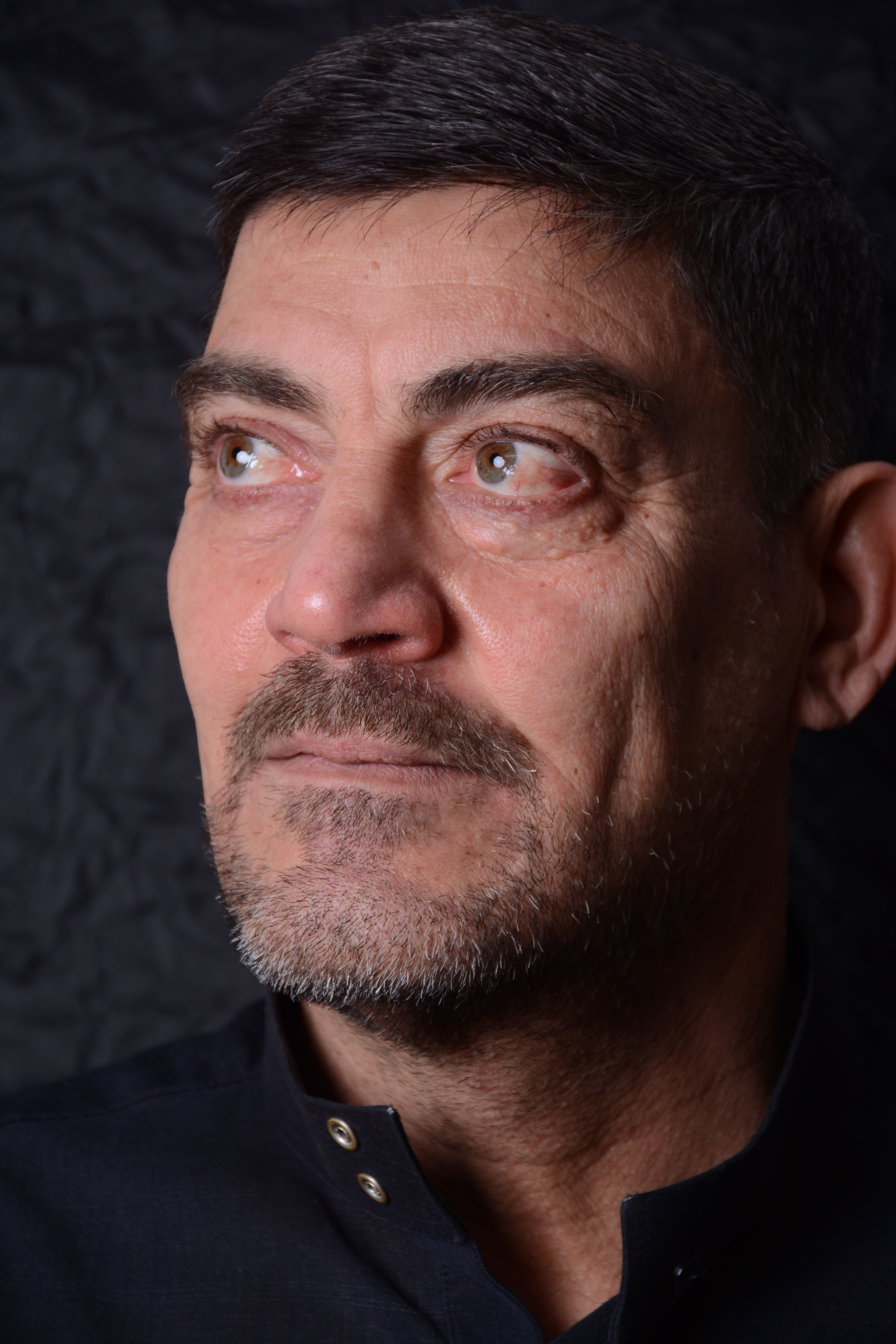 Close-up portrait of a thoughtful bearded man against a dark background.