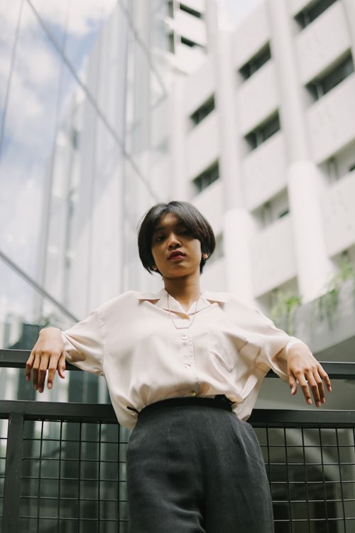 Free A person in elegant attire poses confidently on a balcony against a modern city building background. Stock Photo
