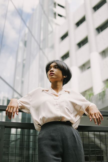 Elegant woman with short hair leaning on a balcony railing in an urban setting.
