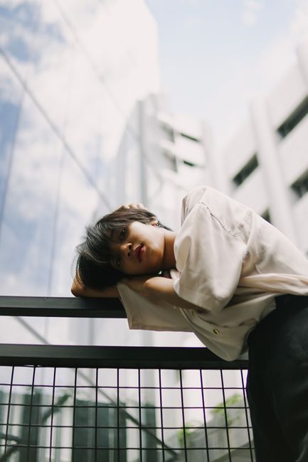 Portrait of an Asian woman leaning on railing with city skyline reflection.