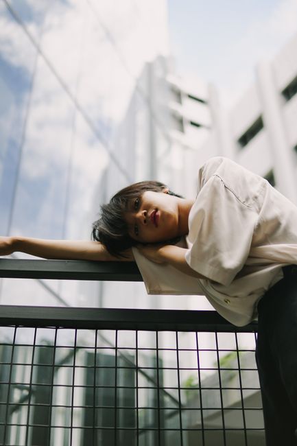 A young woman leans elegantly on a metal railing in a modern urban setting.
