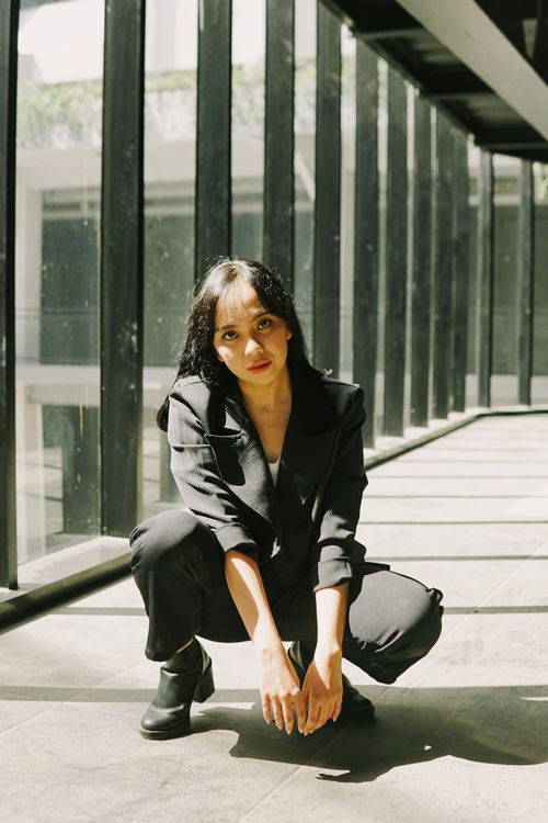 Free A confident businesswoman crouches in a modern glass corridor with sunlight streaming in. Stock Photo