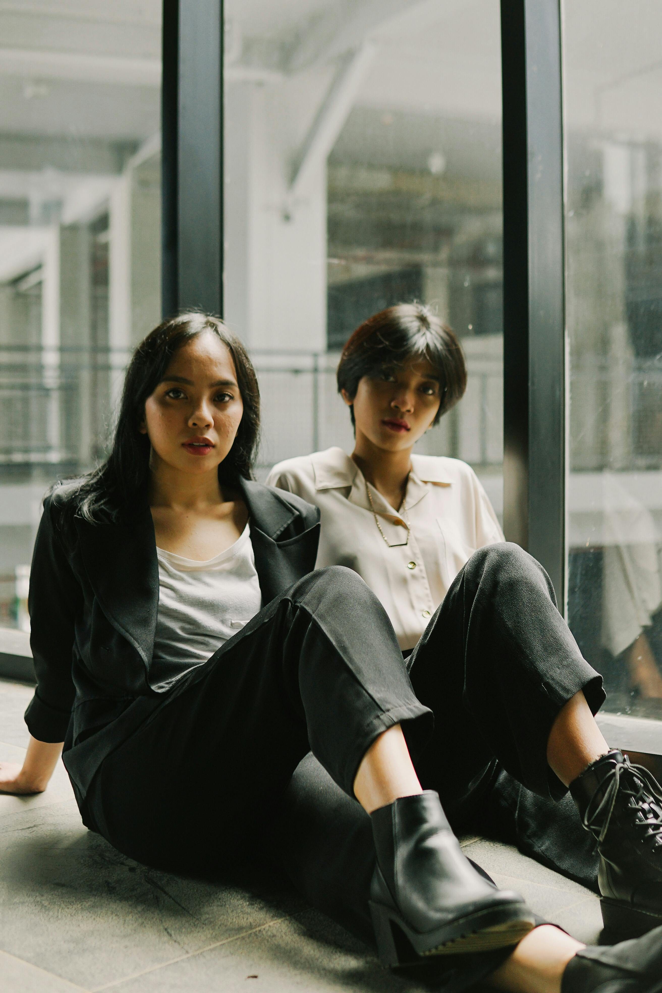 Two young women sitting casually by a window, exuding a confident and relaxed vibe.