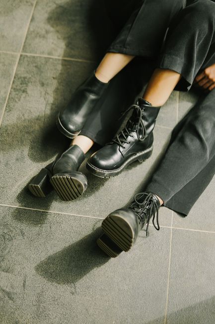 Close-up of two people wearing black boots and pants on a tiled floor.