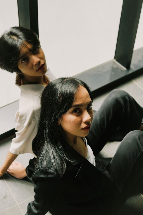 Free Two women sitting on the floor indoors, posing near a large window. Stock Photo