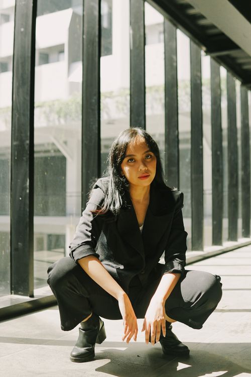 Free Stylish woman in a black outfit confidently poses in a sunlit, modern urban space. Stock Photo