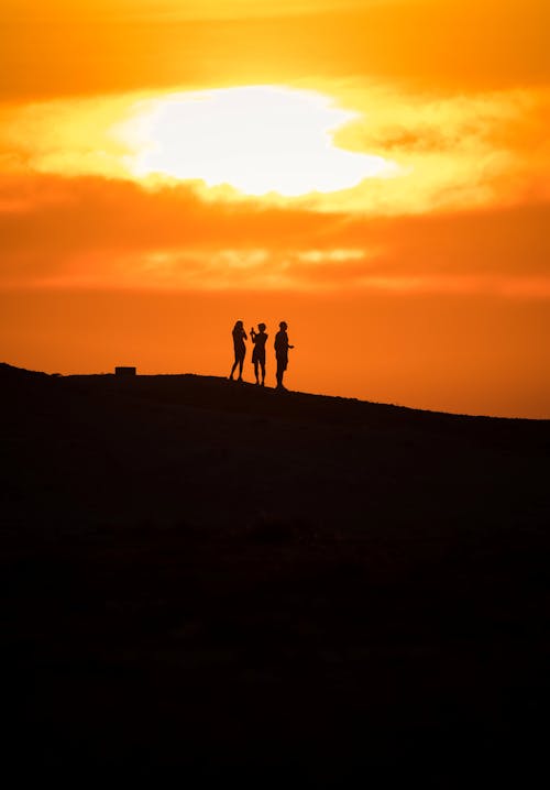 Silhouette of Three People Standing on the Mountain during Sunset