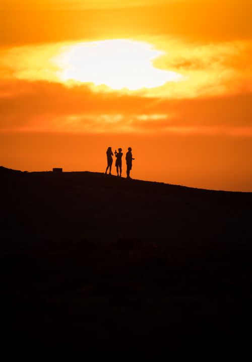 Free Silhouette of three people standing on a hill at sunset, creating a dramatic scene. Stock Photo