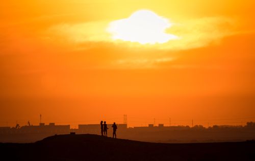 Free Silhouettes of three people under a vivid orange sunset, capturing the essence of golden hour. Stock Photo