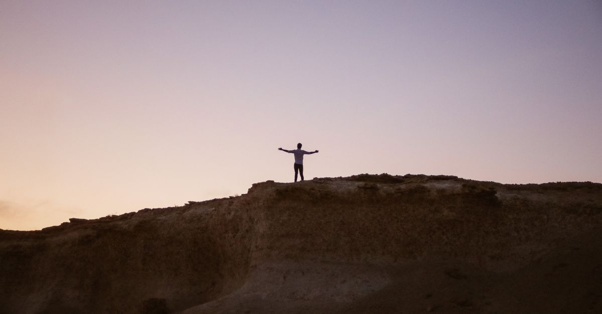 person standing on a cliff edge at sunset, looking into a glowing horizon