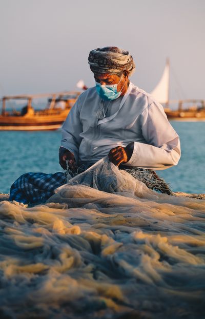 A fisherman in traditional clothing repairing his net by the sea