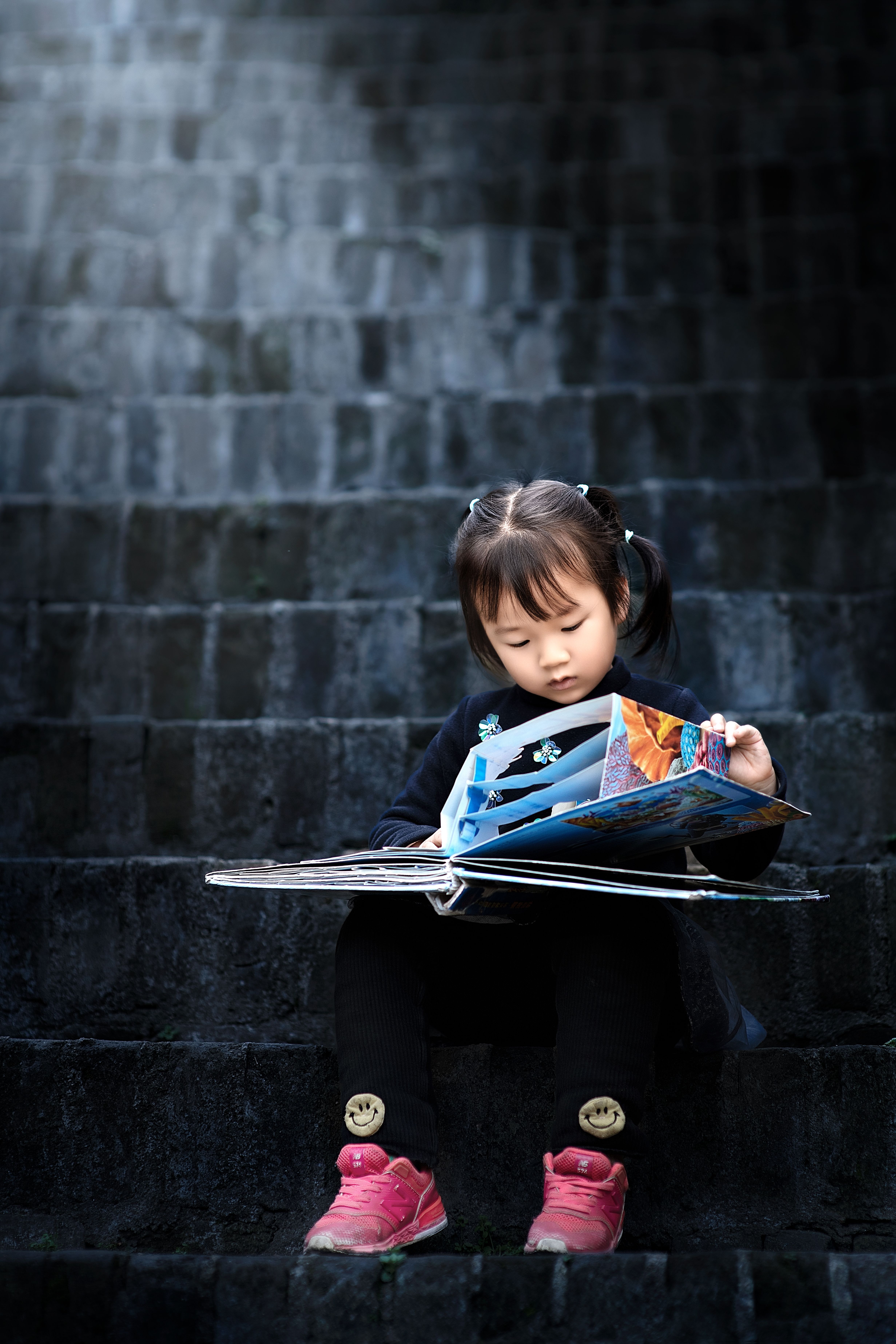 Little girl engrossed in reading a book while sitting on outdoor stone stairs.