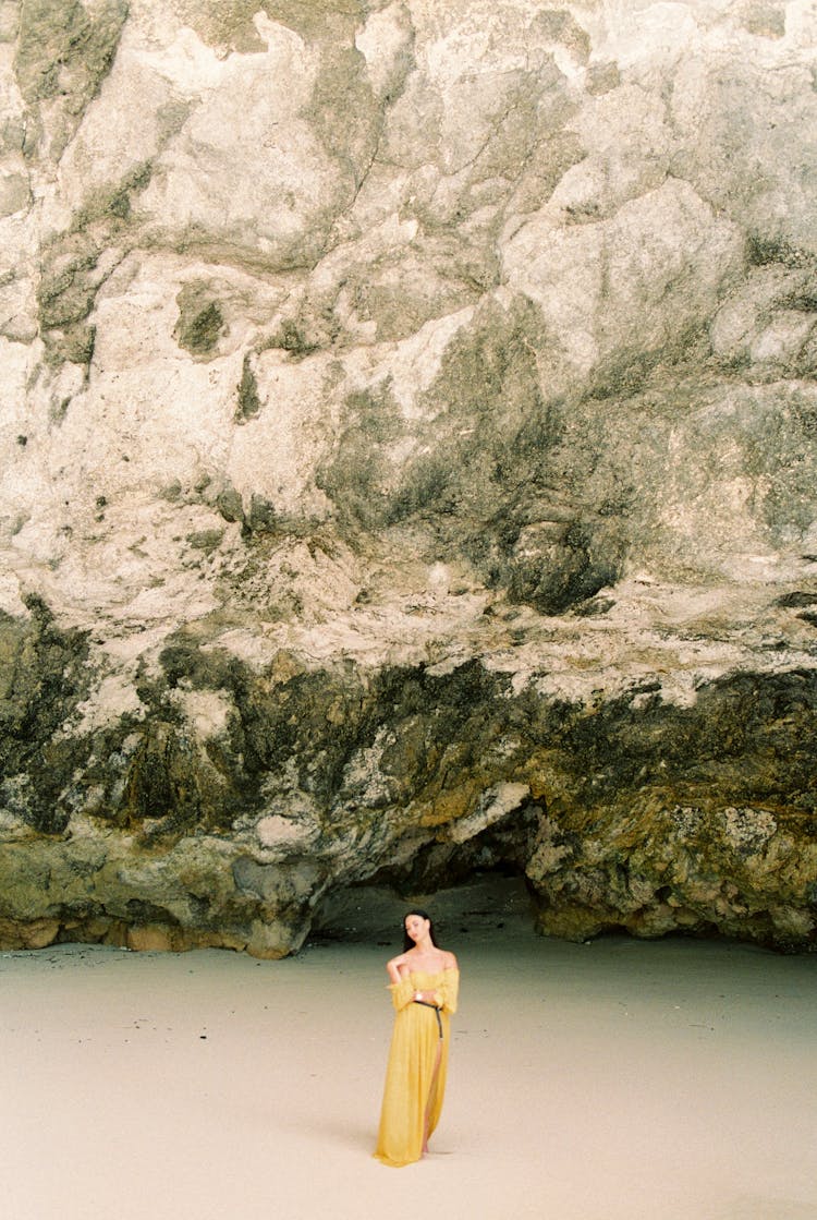 Woman In Yellow Dress Standing Under Cliff Wall