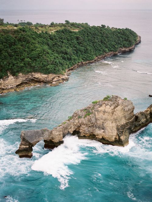 Free Experience the breathtaking rocky coastline of Bali with crashing waves against lush green cliffs. Stock Photo